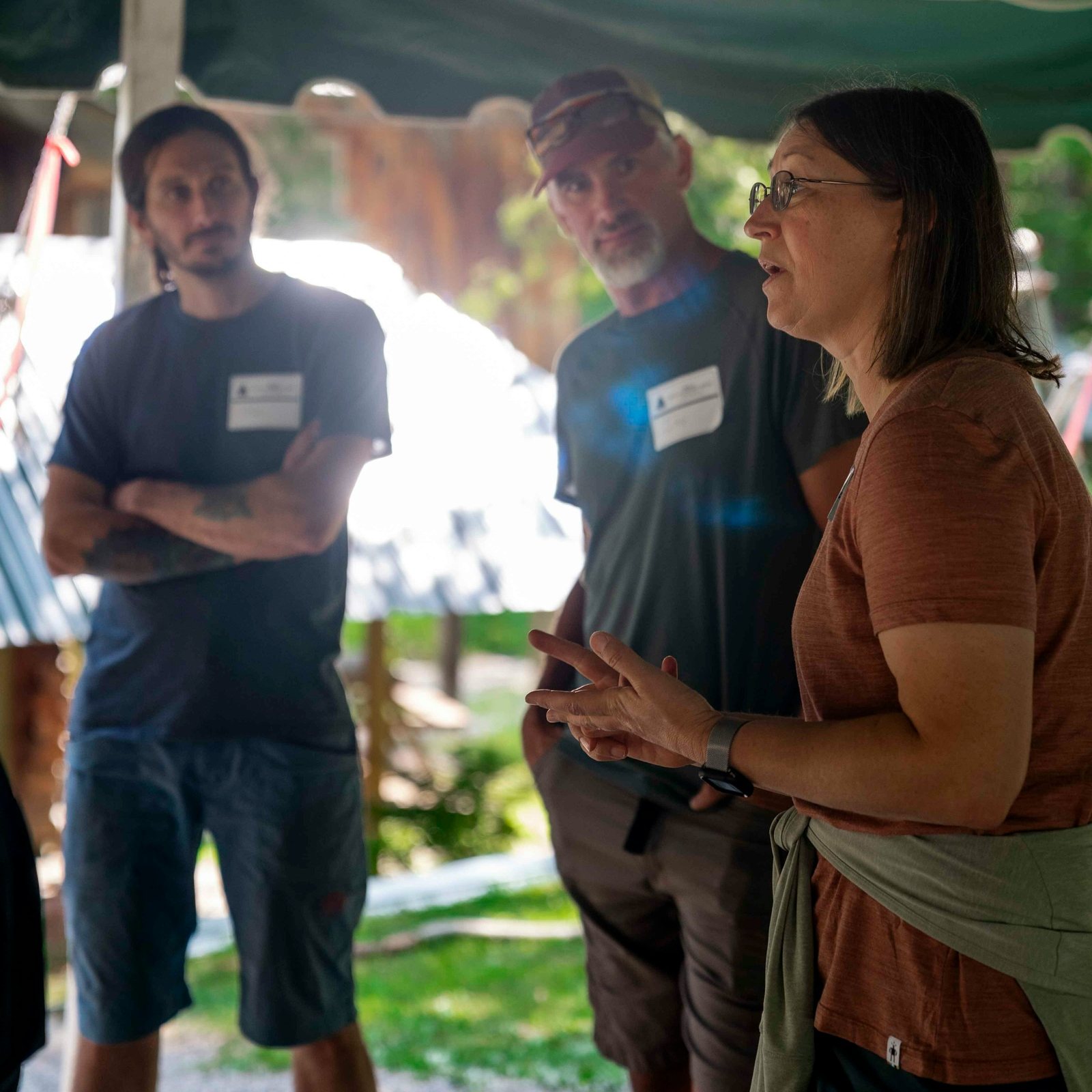 Three people in conversation under a shaded tent